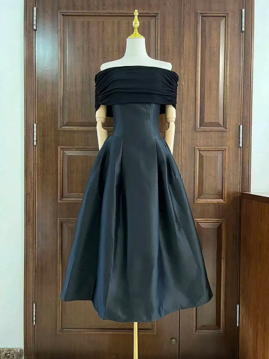 Black off-shoulder gown on a mannequin against a wooden door background