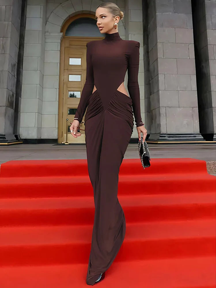 Woman in a brown dress standing on a red carpet in front of a building entrance.