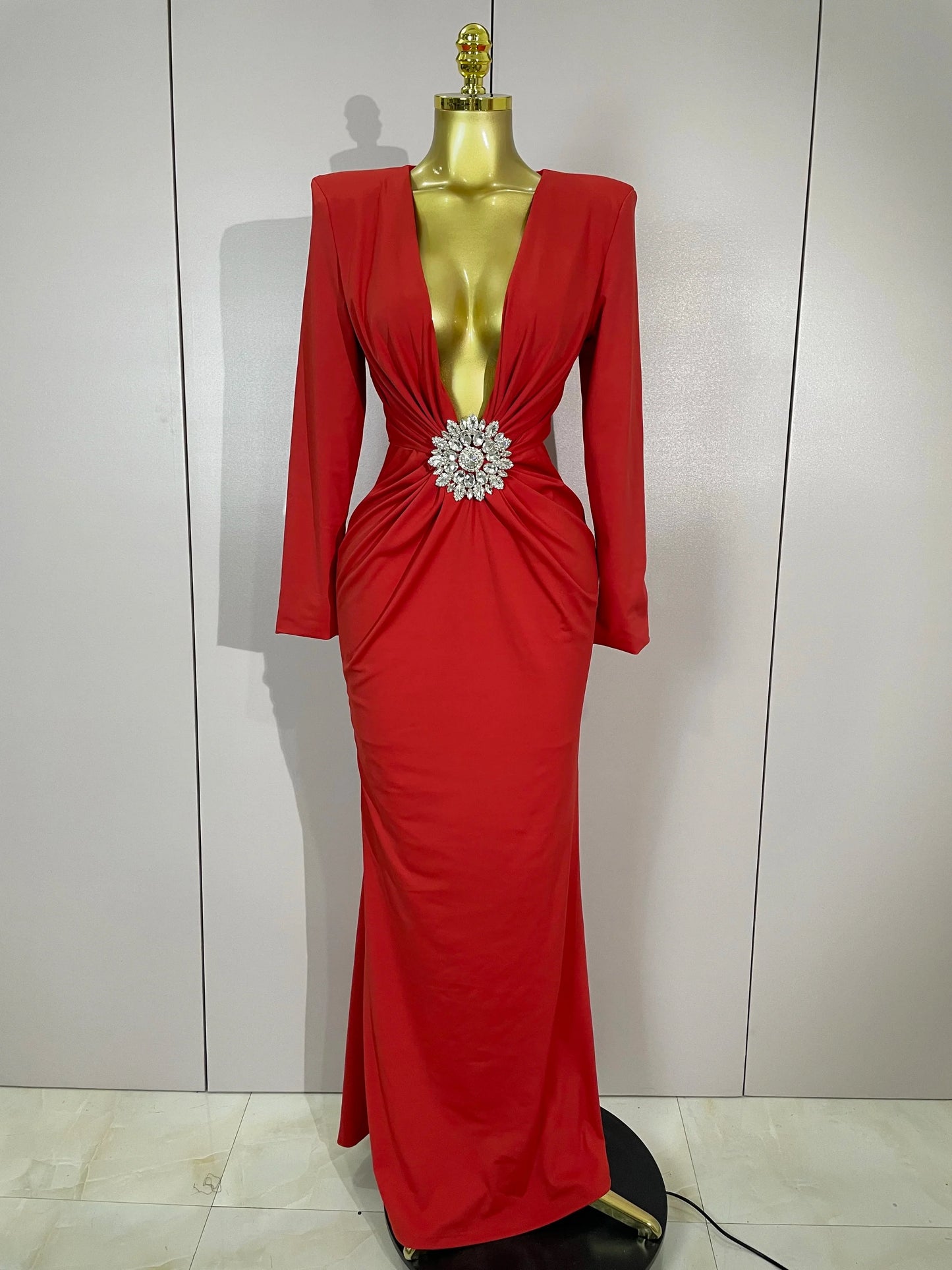 Red evening gown with a large brooch on a mannequin against a white background