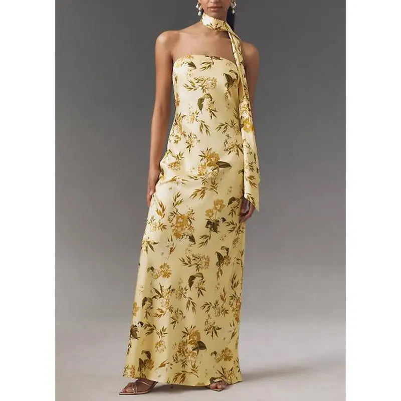 A woman wearing a flowy long summer dress, worn with minimal sandals, with a plain background