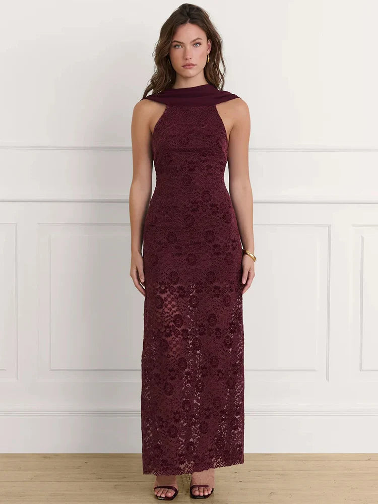 Woman wearing a burgundy lace dress against a white wall.