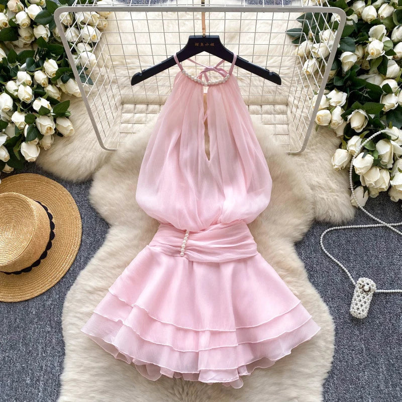 Pink dress on a hanger with flowers and a hat in the background