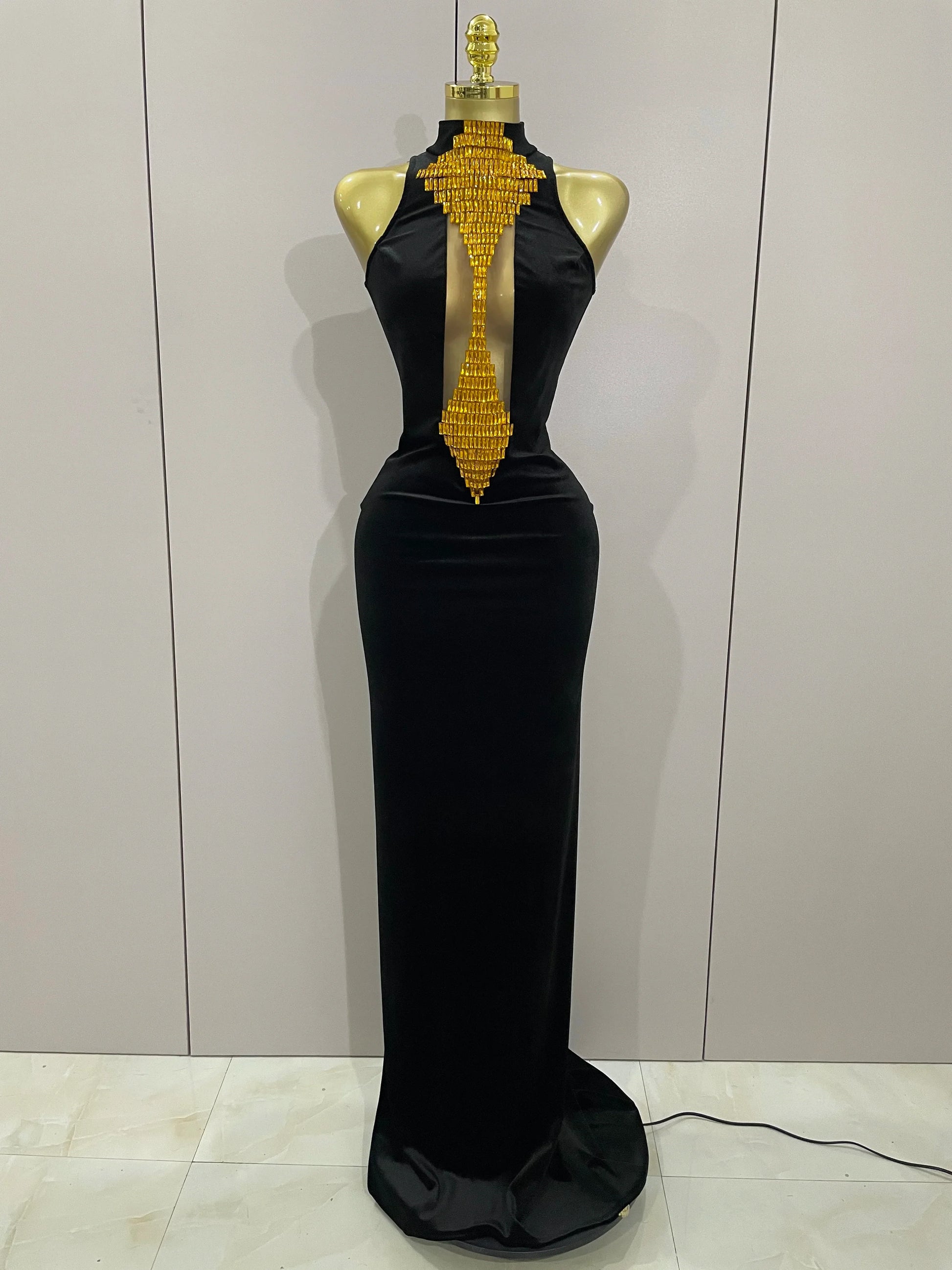 Black evening gown with gold embellishments on a mannequin against a white wall.