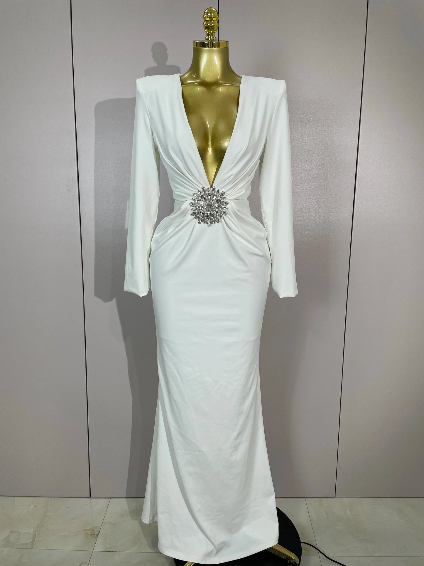 White evening gown with a silver brooch on a mannequin against a plain background