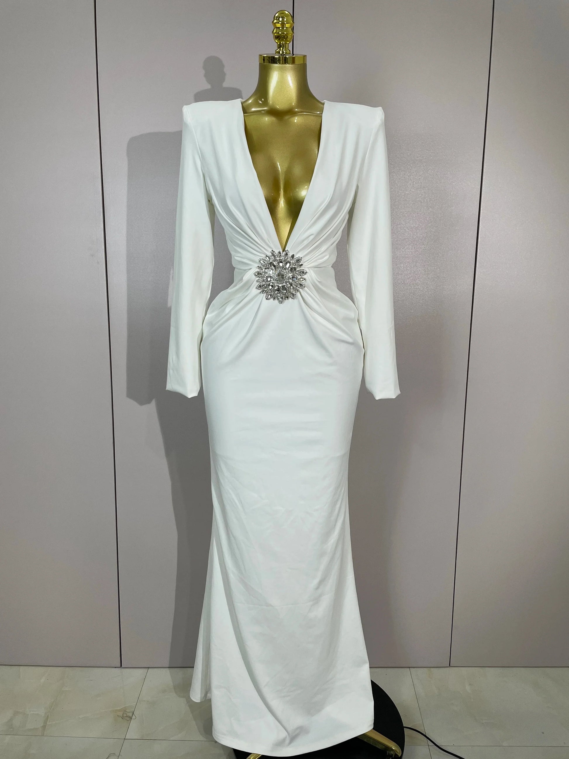 White evening gown with a silver brooch on a mannequin against a plain background