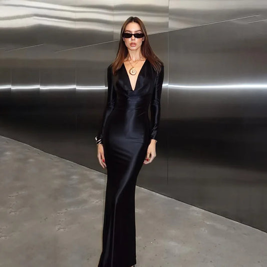 Woman in a black satin dress standing against a reflective metallic wall.