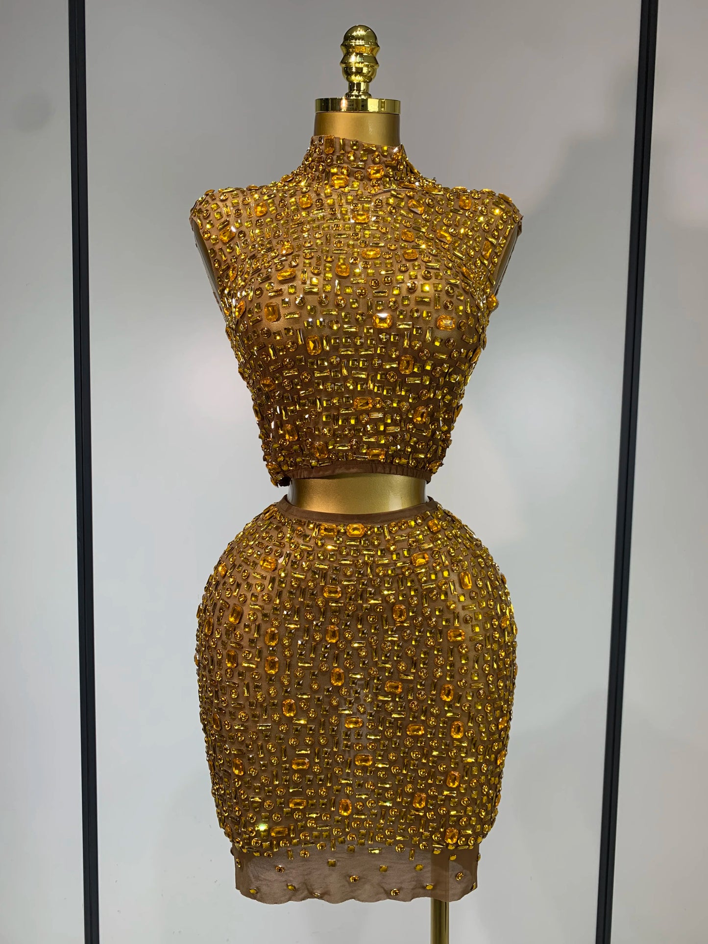 Gold beaded dress form against a neutral background