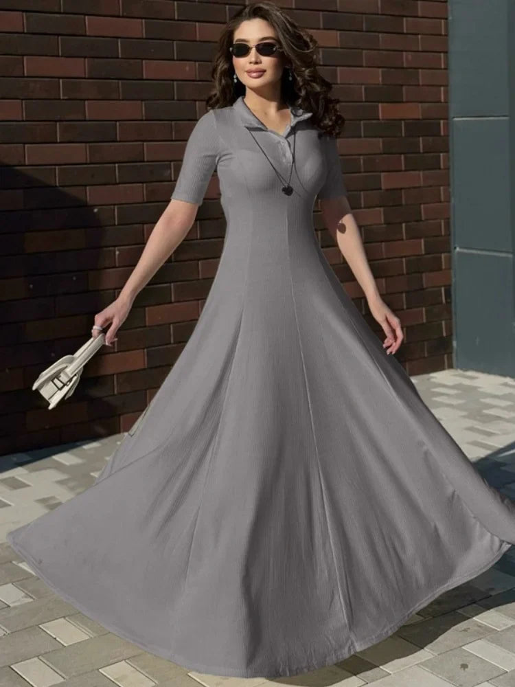 Woman in a gray dress standing against a brick wall.