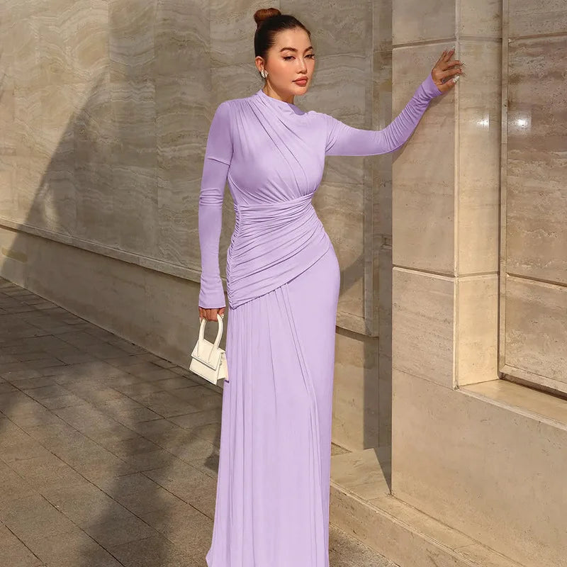Woman in a long purple dress standing against a stone wall.