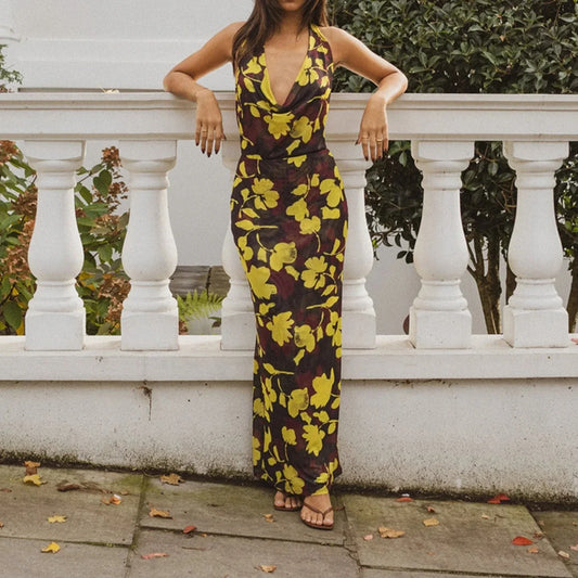 A woman wearing a yellow and brown floral dress is standing against a white railing.