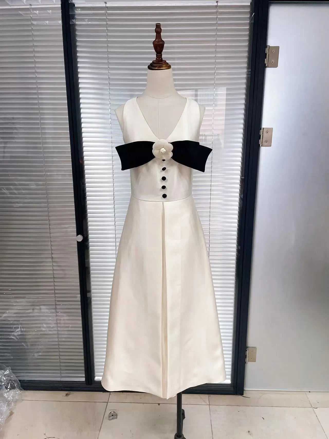 White dress with black bow on a mannequin against a glass door background