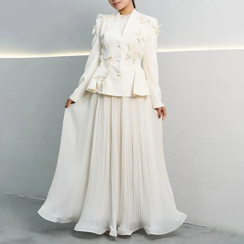 Woman wearing a white outfit with a jacket and long skirt against a plain background