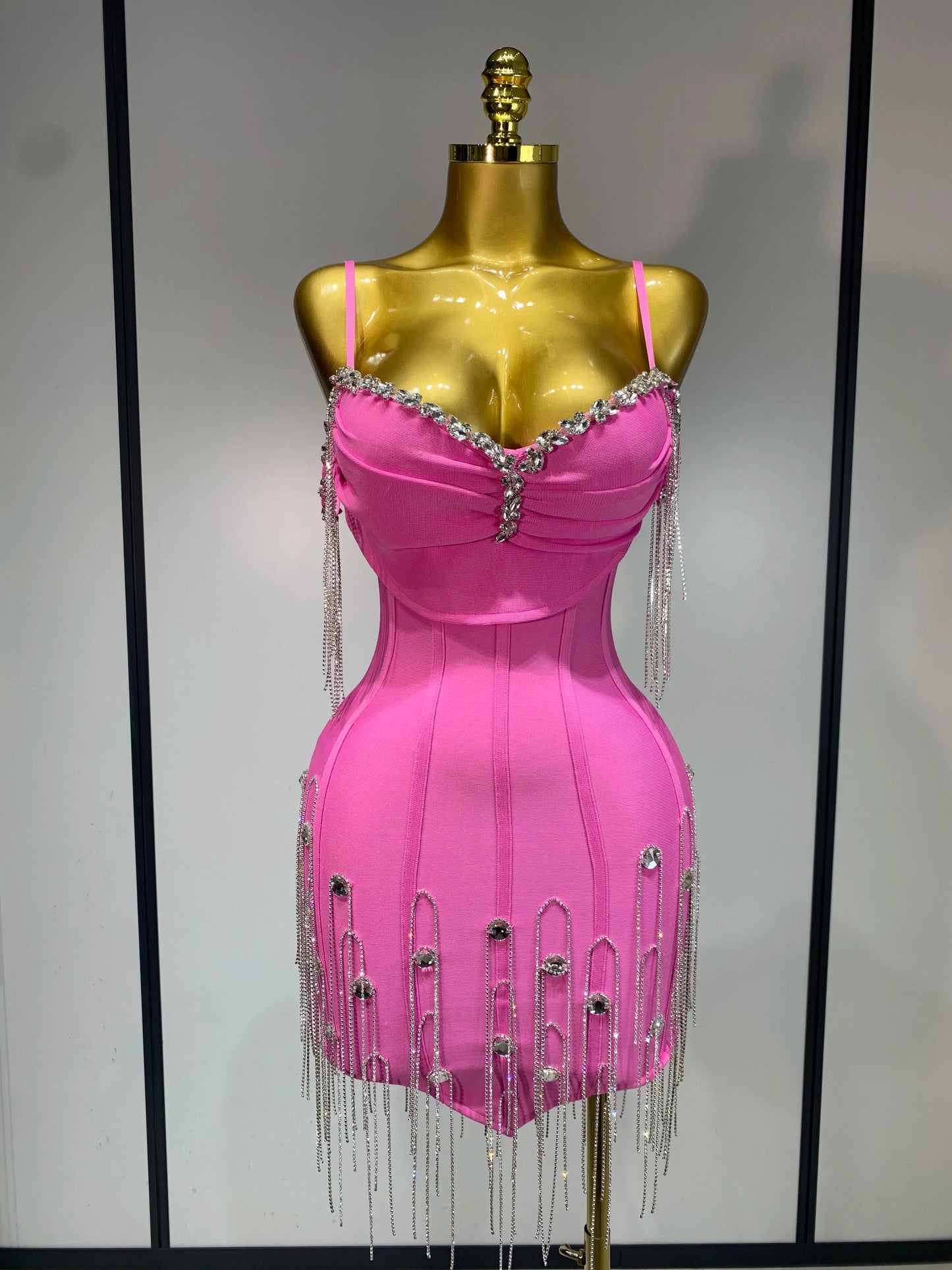 Pink dress with fringe and embellishments on a gold mannequin against a plain background