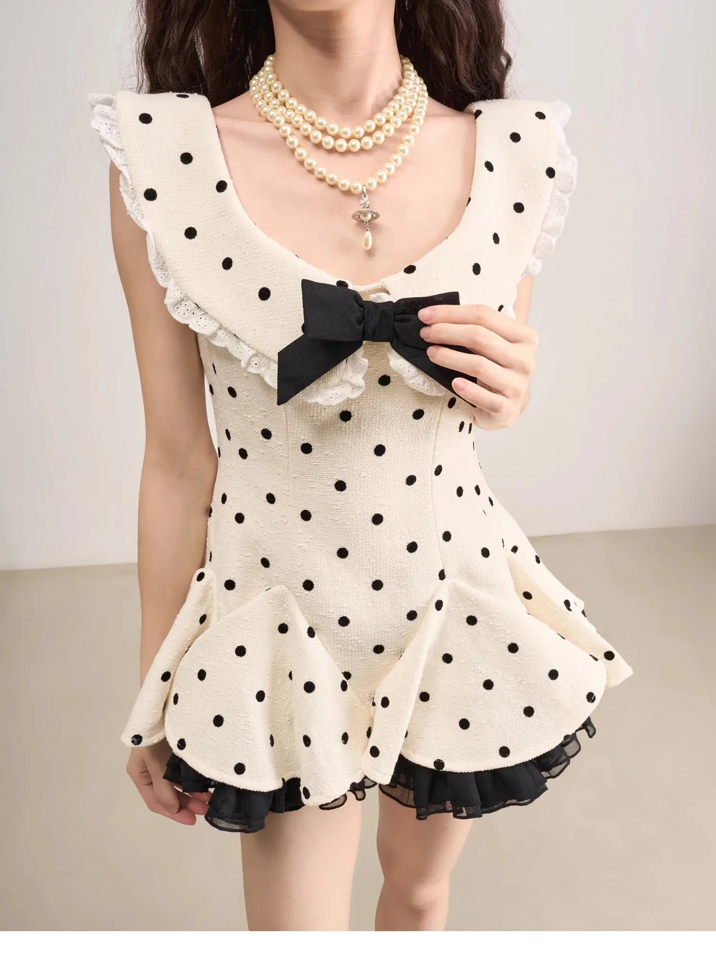 Woman wearing a polka dot dress with a black bow and pearl necklace on a plain background
