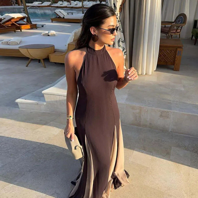Woman in a long, halter-neck dress standing by a poolside.