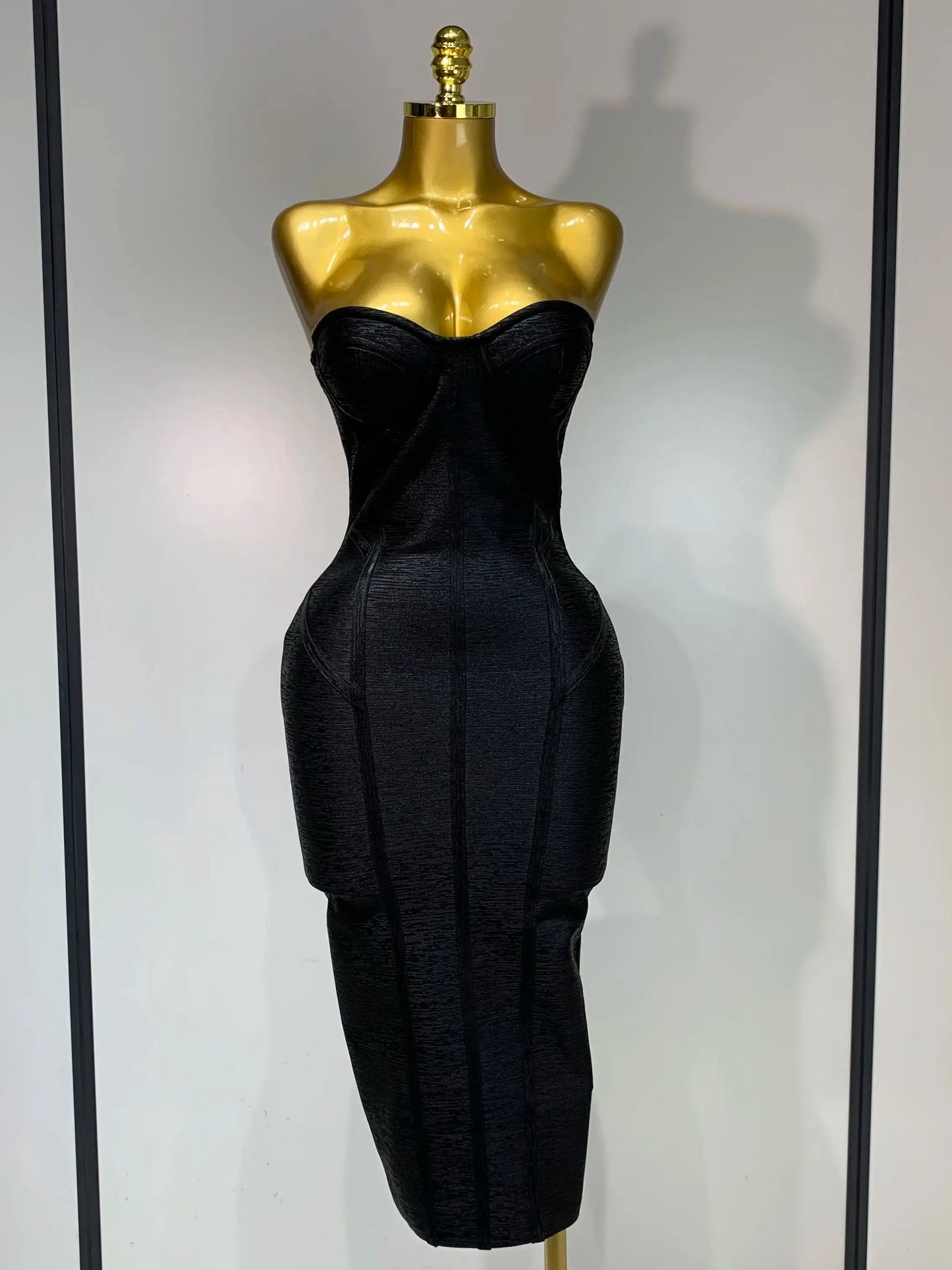 Black strapless dress on a gold mannequin against a white background