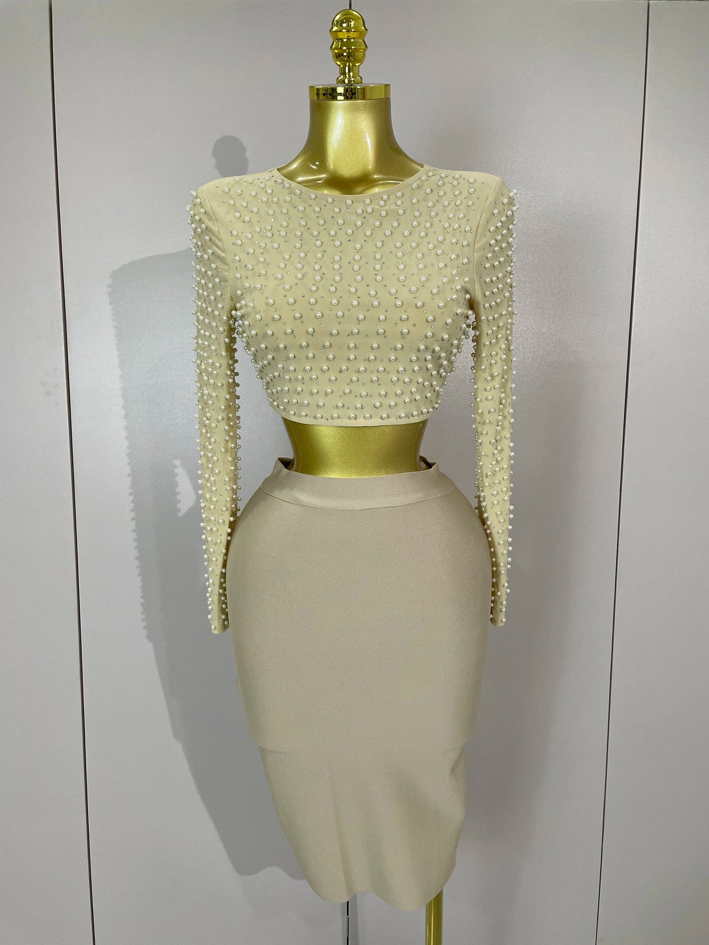 Mannequin wearing a beige dress with pearl embellishments and a skirt against a white background