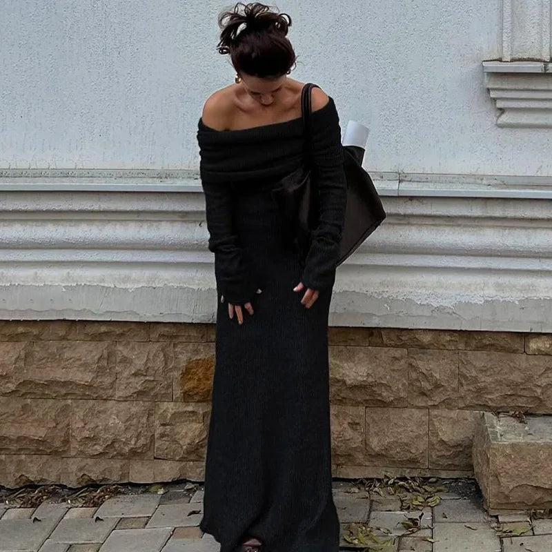 Woman in a black off-shoulder dress standing against a light-colored wall.