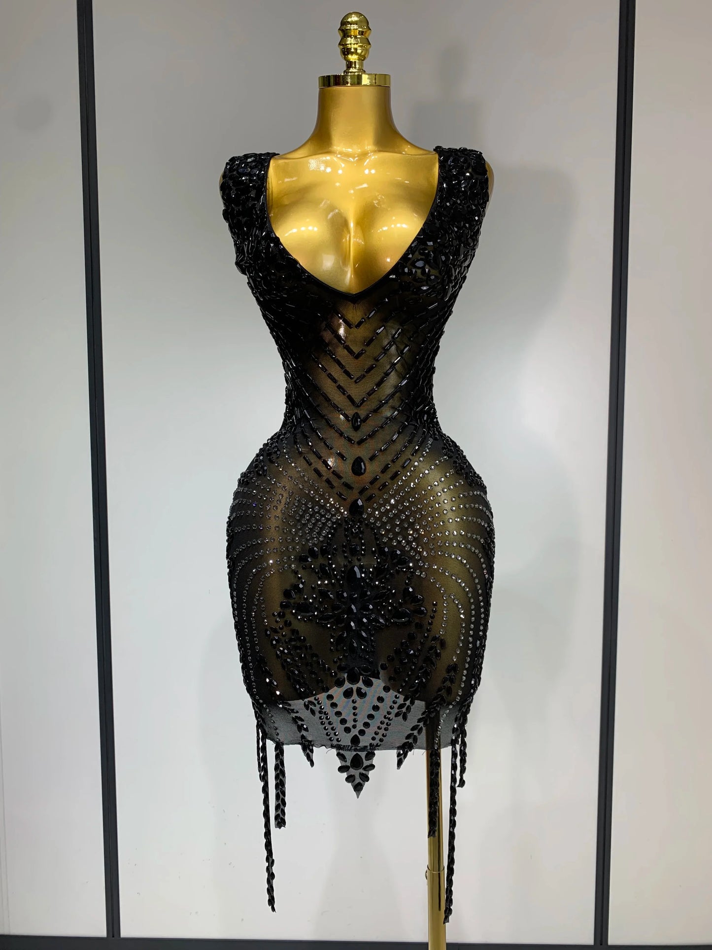 Black beaded dress on a mannequin against a plain background
