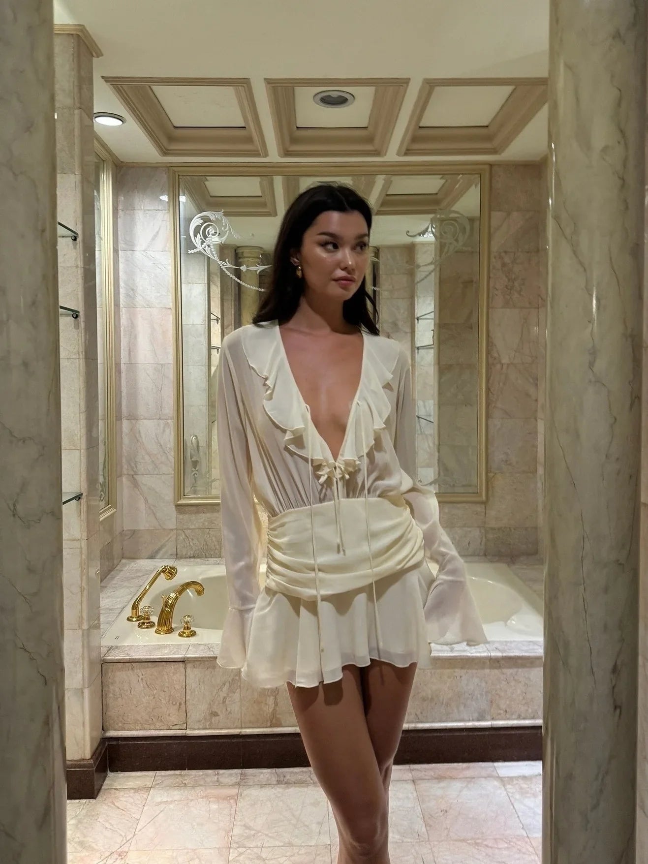 Woman in a white dress standing in a bathroom.