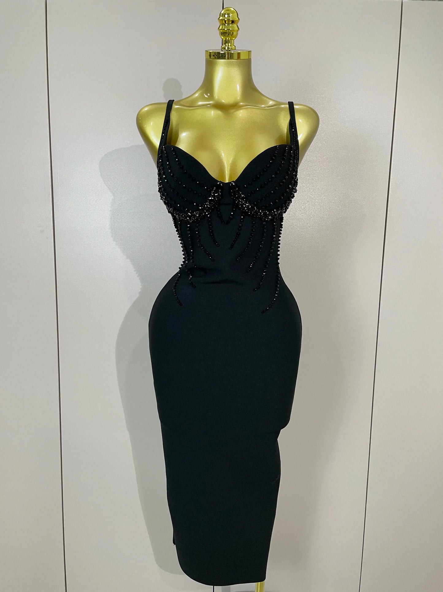 Black dress with bead detailing on a mannequin against a white background