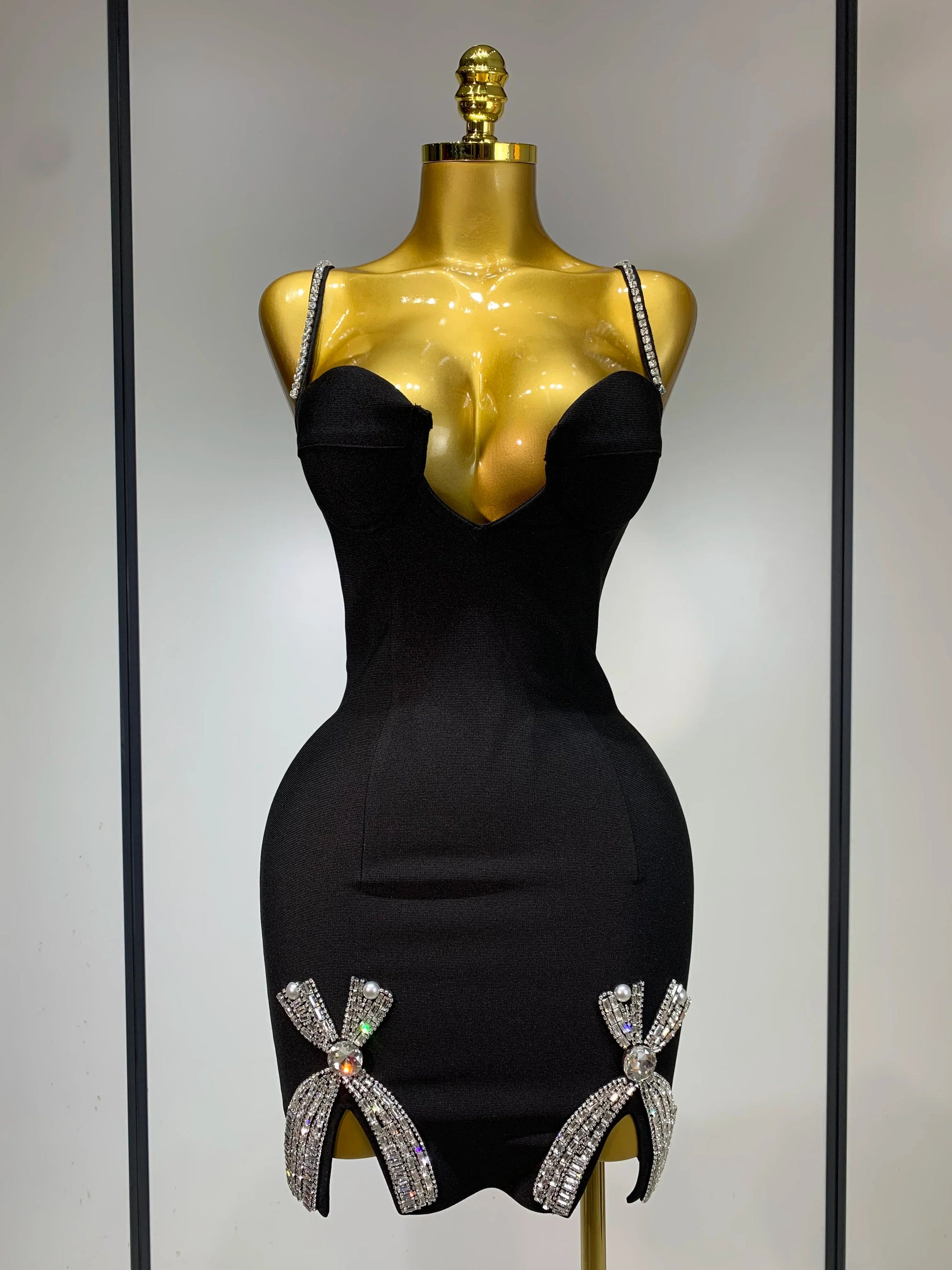 Black dress with decorative bows on a gold mannequin against a neutral background