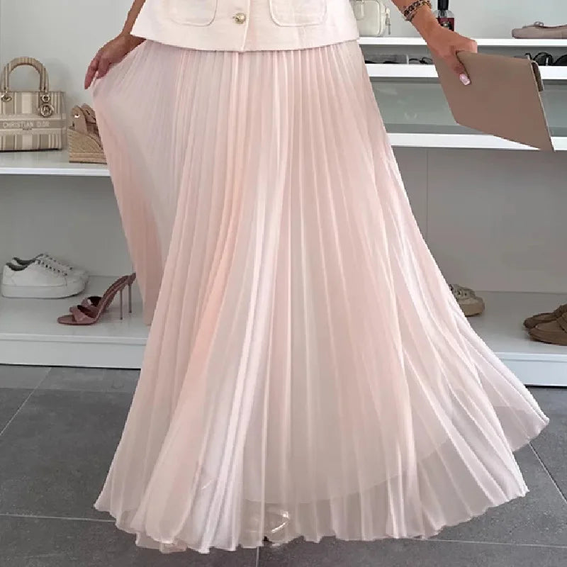 Person wearing a light pink pleated skirt with a blurred background of shoes and bags.