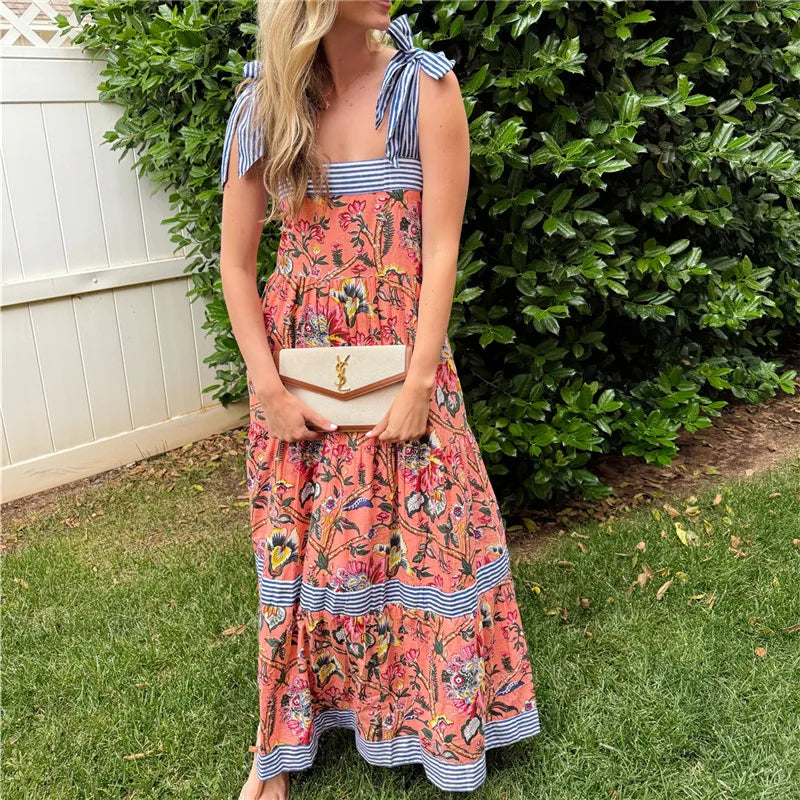 Woman wearing a colorful dress with a floral pattern and striped accents, standing outdoors.