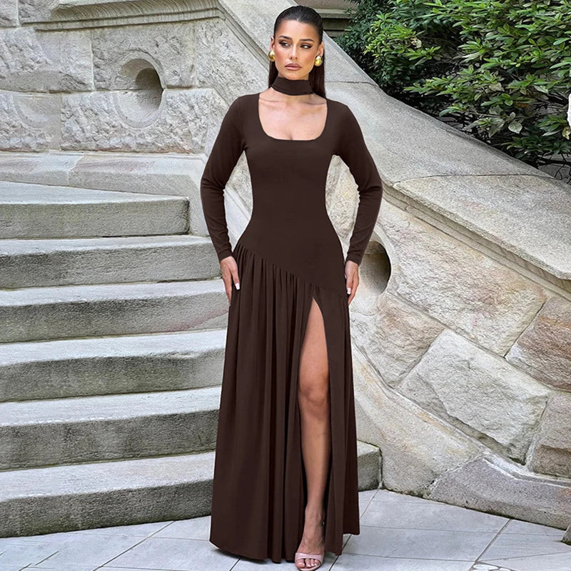 Woman in a brown dress standing on stone steps with a stone wall and greenery in the background