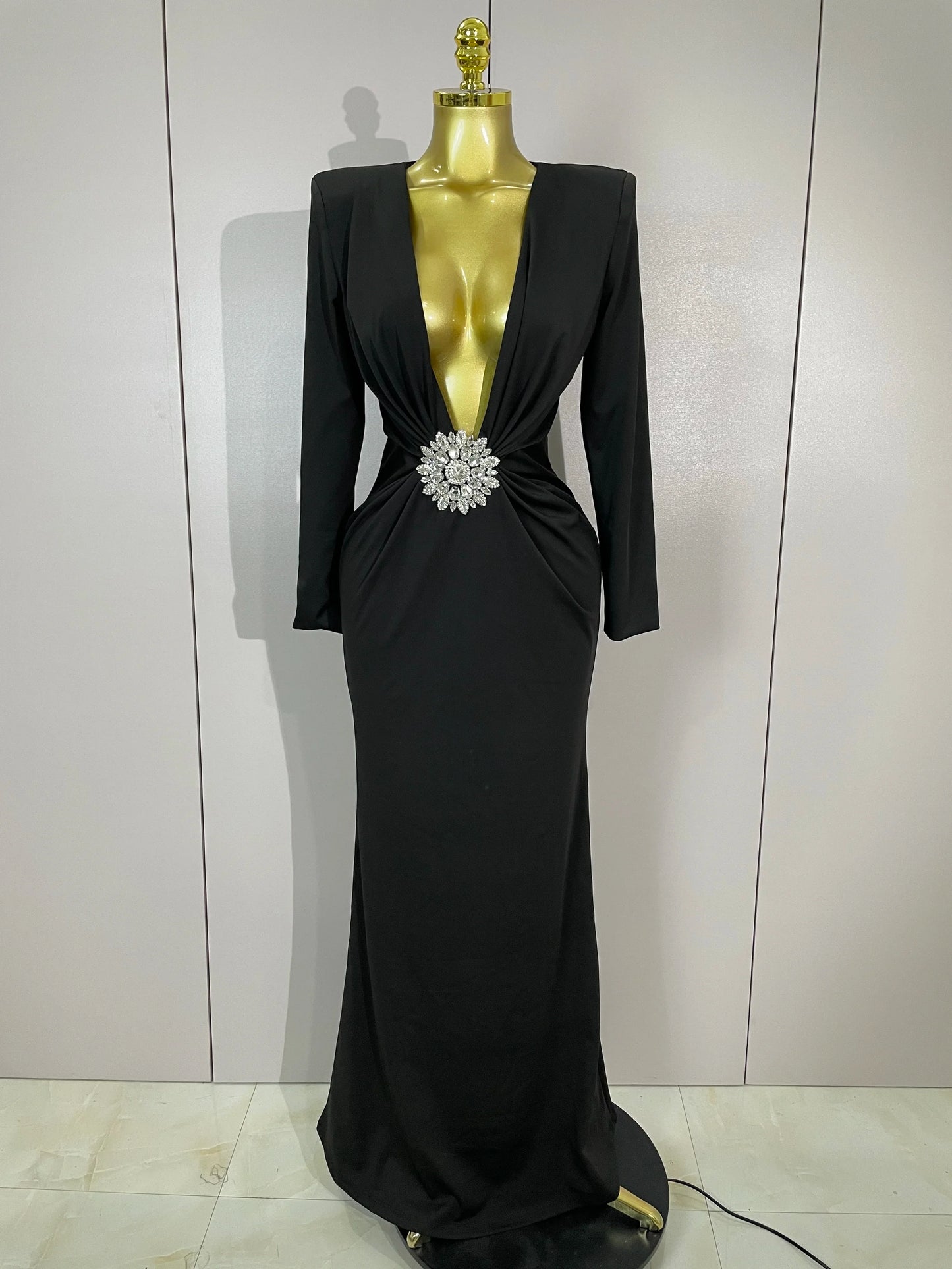 Black evening gown with a large brooch on a mannequin against a white background