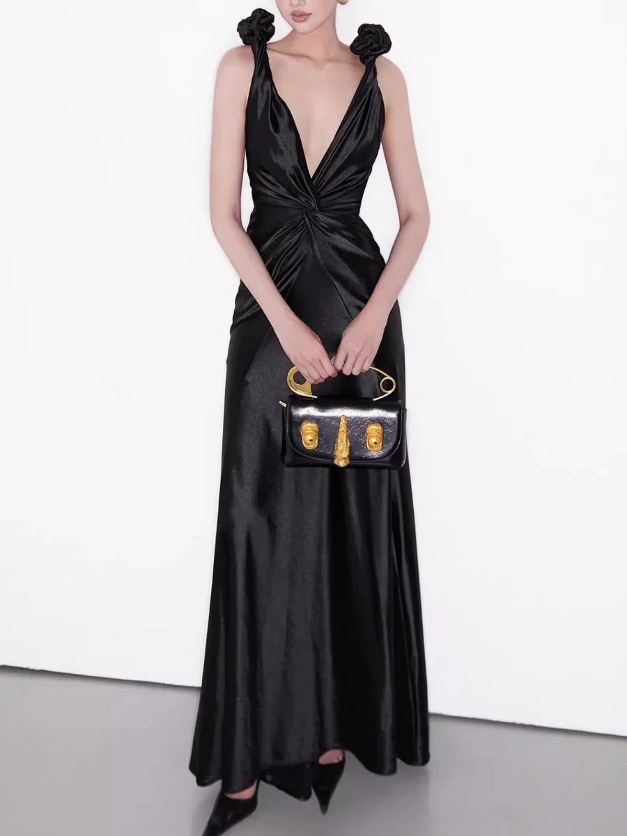 Woman in a black satin dress holding a matching handbag against a white background