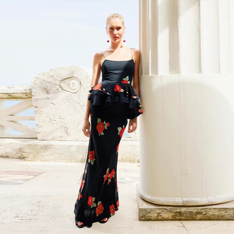 Woman in a black floral dress standing next to a white column with a clear sky background