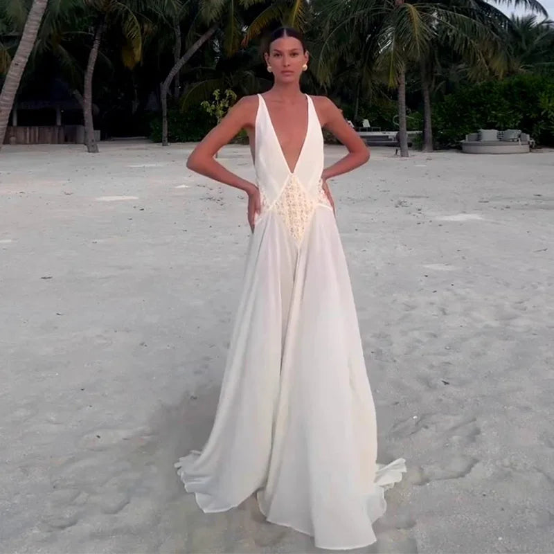 Woman in a white evening gown with a deep neckline on a sandy beach.