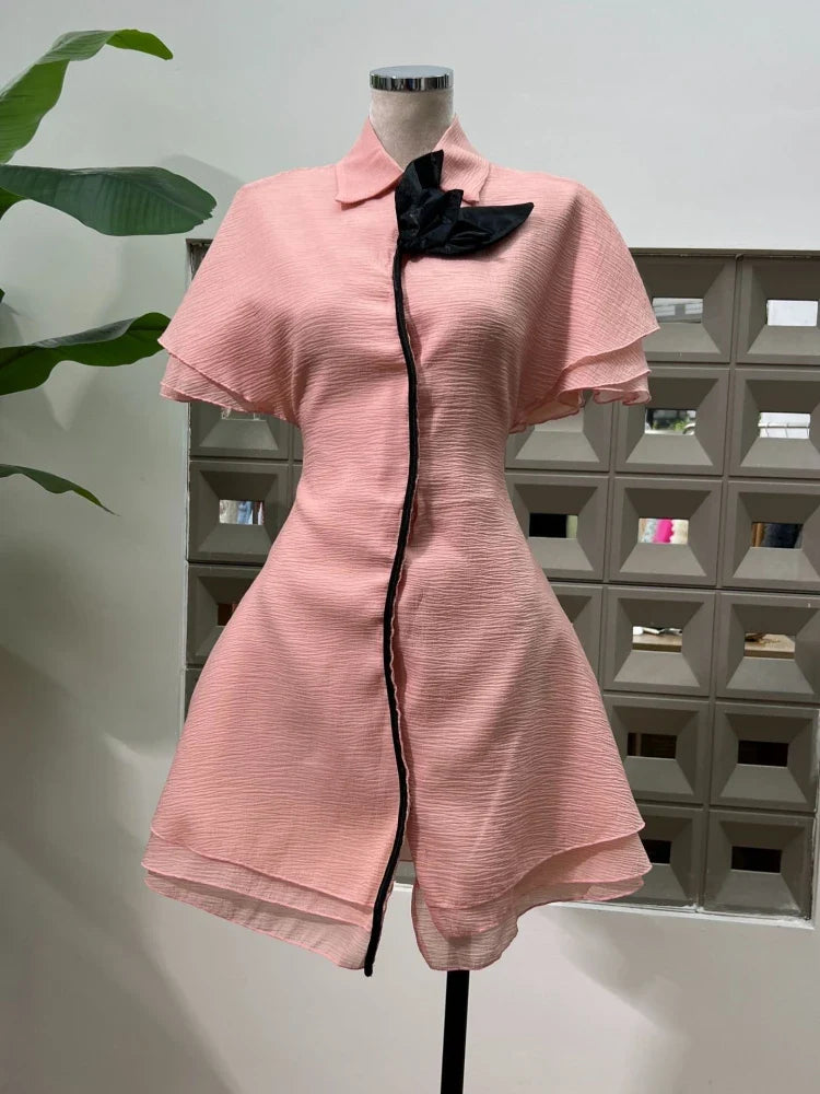 Pink dress with black trim on a mannequin against a geometric wall.